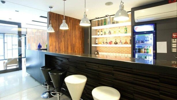 A modern bar area with a wooden accent wall, black bar stools, and pendant lighting. - At One (Bangkok)