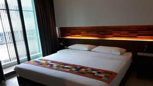 A hotel room with a large bed, a wooden headboard, and a window with blinds. - At One (Bangkok)