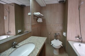 Une salle de bain équipée d’un lavabo, de toilettes et d’une baignoire. On y trouve un porte-serviettes avec des serviettes, un miroir et une pomme de douche.