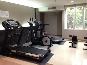 Ein Fitnessstudio mit Laufbändern, Crosstrainern und Langhantelbänken.