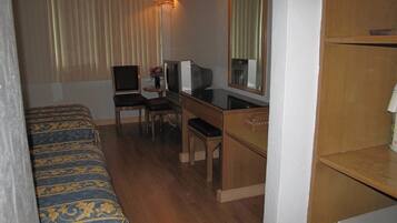 A hotel room with a bed, a desk with a computer, a chair, a television, and a mirror.