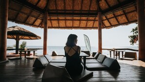 A covered outdoor seating area with a view of the sea, featuring thatched roof, wooden furniture, and a table with a flag. - Nature Beach Resort (Ko Chang)