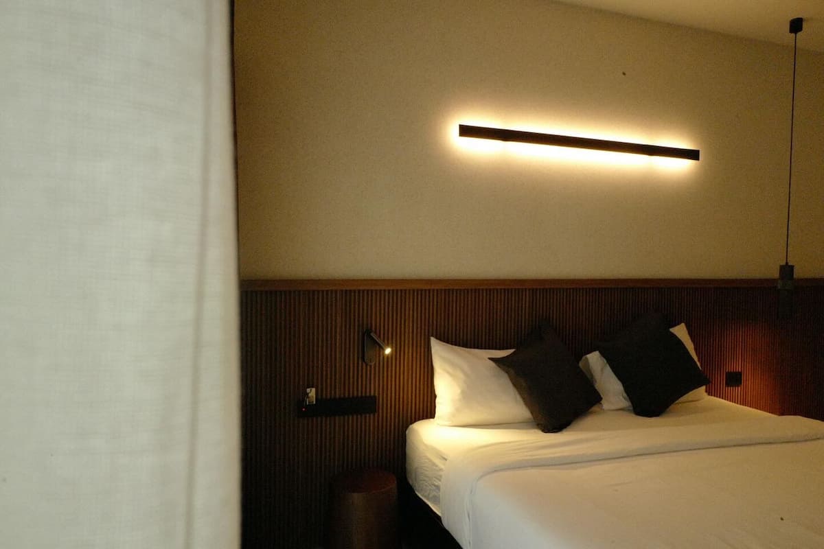 A hotel room with a bed, a bedside table, a lamp, and a wall-mounted light fixture.