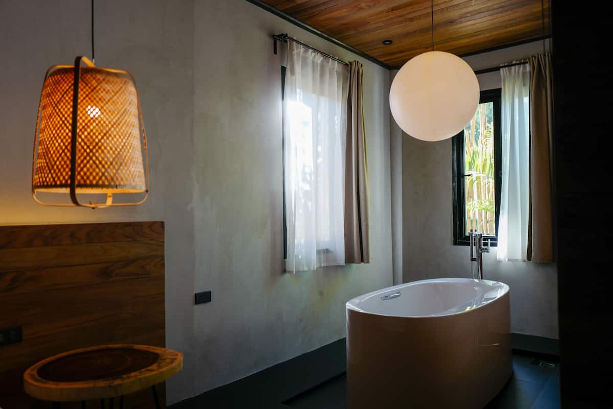 A modern bathroom with a freestanding bathtub, wooden accents, and a large pendant light.