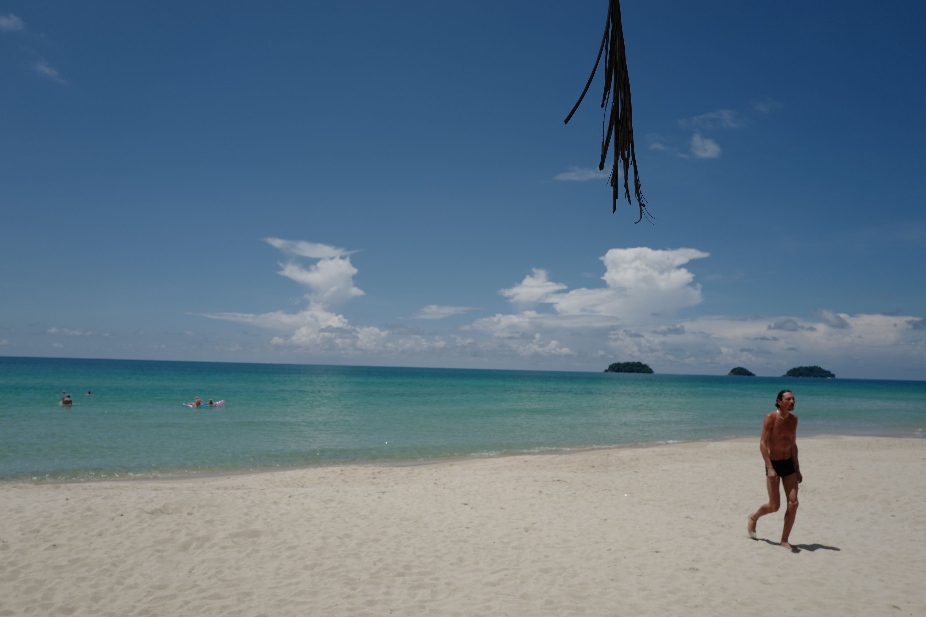 A beach with clear blue water, a sandy shore, and a person walking.