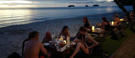 Un área de comedor frente a la playa, con mesas y sillas, con vista al mar.