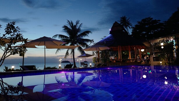 A poolside area with umbrellas, lounge chairs, and a view of the ocean at dusk. - Nature Beach Resort (Ko Chang)