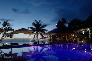 A poolside area with umbrellas, lounge chairs, and a view of the ocean at dusk. - Nature Beach Resort (Ko Chang)