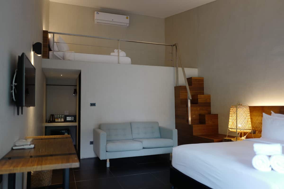 A modern hotel room with a bunk bed, a sofa, a bedside table, a lamp, and a TV.