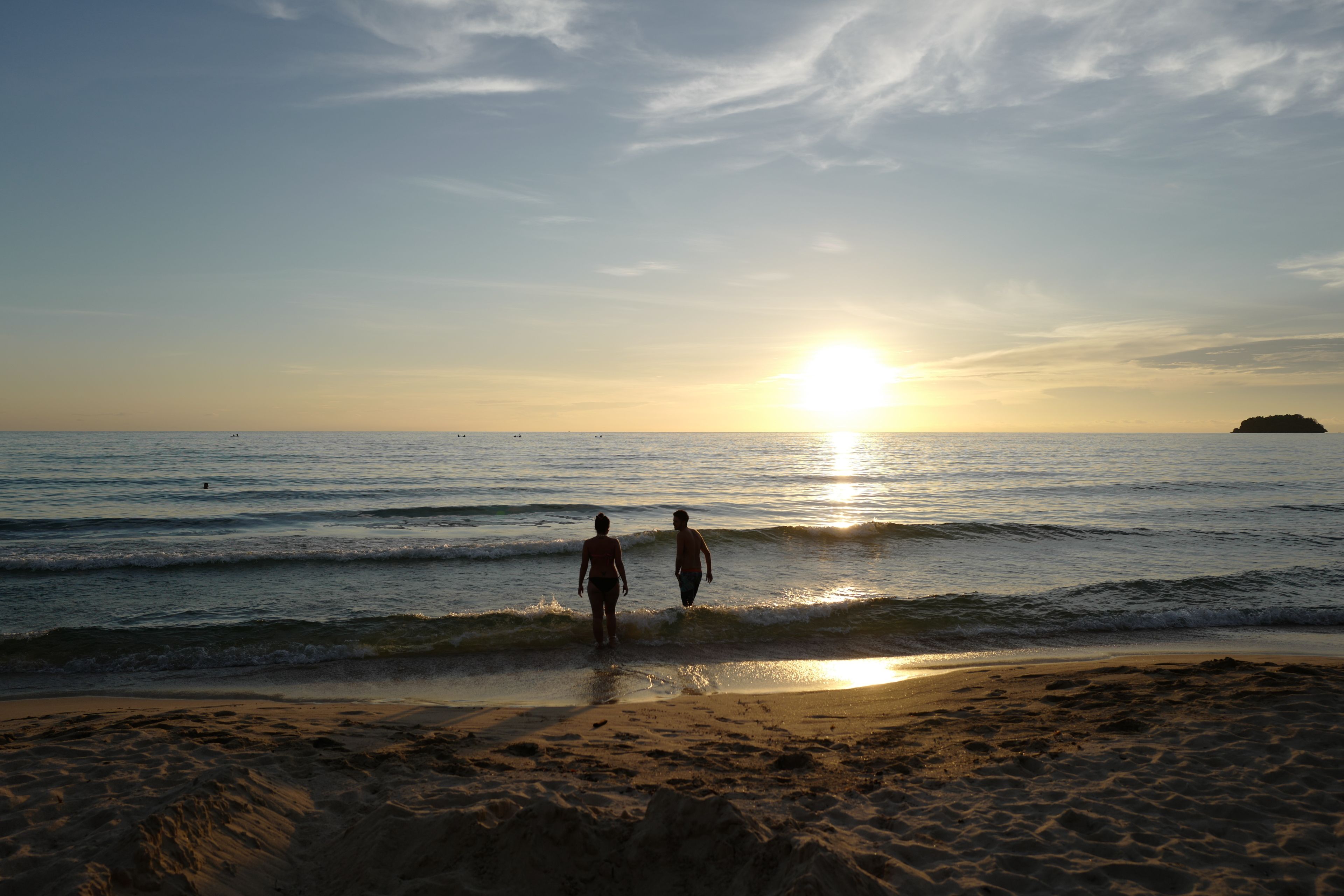 A beach with two people walking towards the sunset.