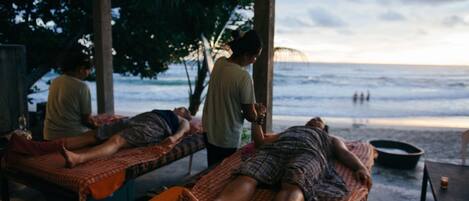 A massage parlor with two massage tables under a covered area, overlooking a beach.