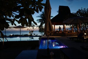 A pool area with lounge chairs and umbrellas, overlooking a body of water at dusk. - Nature Beach Resort (Ko Chang)
