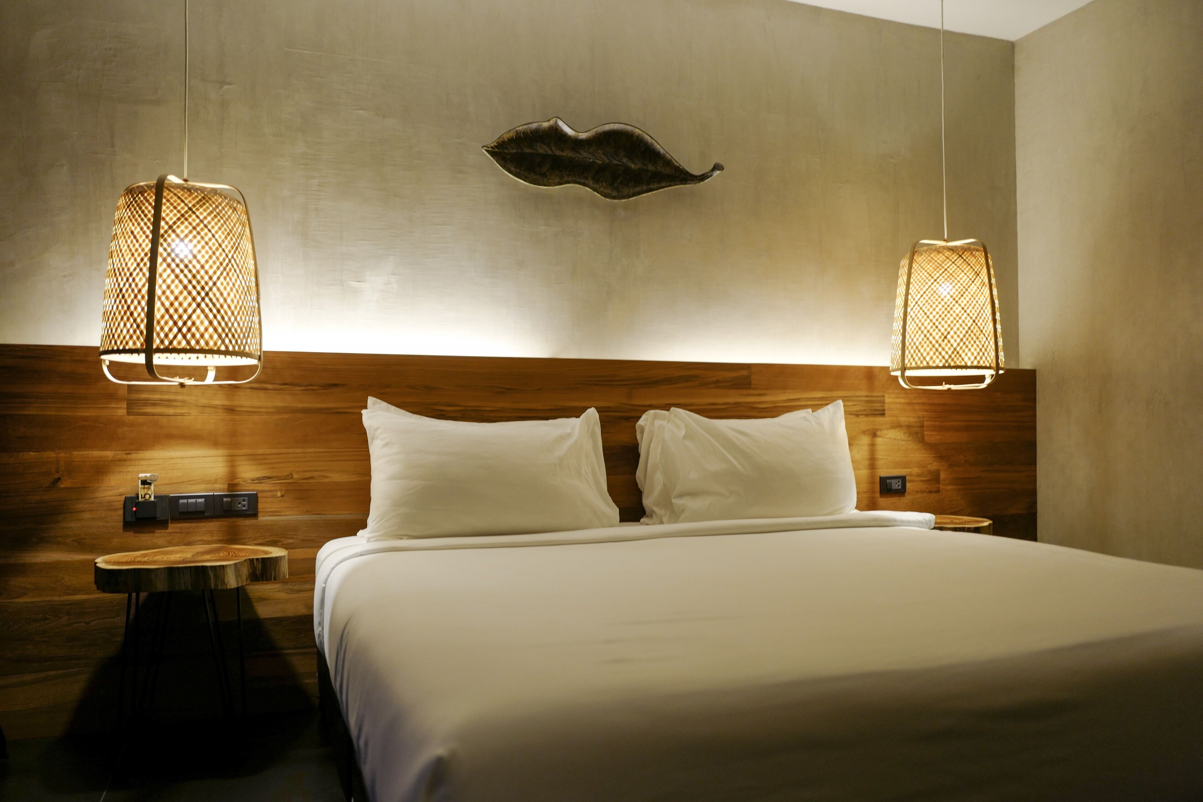 A neatly made bed with white linens, two wall-mounted lamps with a woven design, and a wooden headboard.