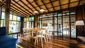 A spacious room with a wooden ceiling, large windows, a dining table with chairs, and a blue sofa. - Nature Beach Resort (Ko Chang)