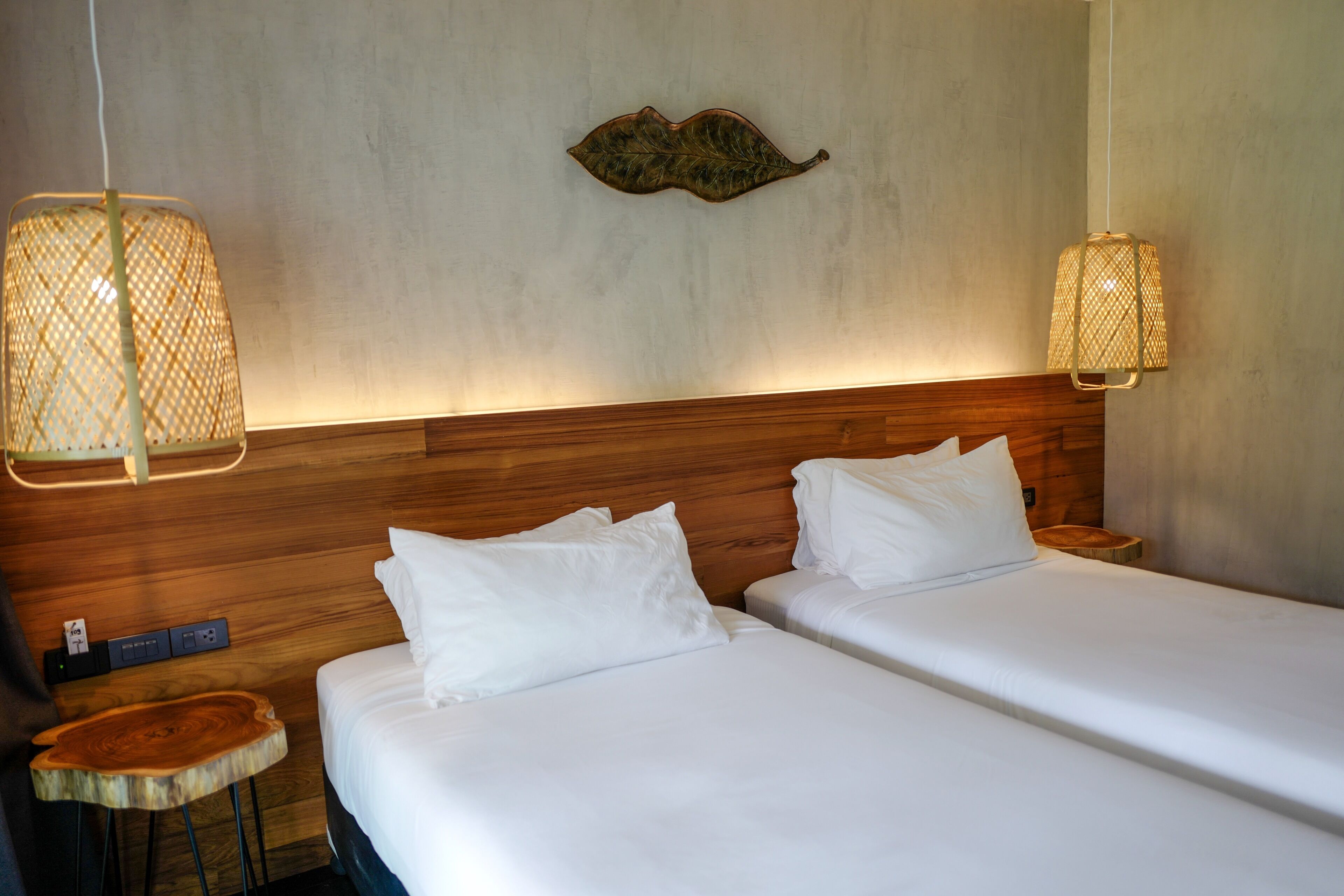 A hotel room with two beds, wooden headboard, and two hanging lamps.