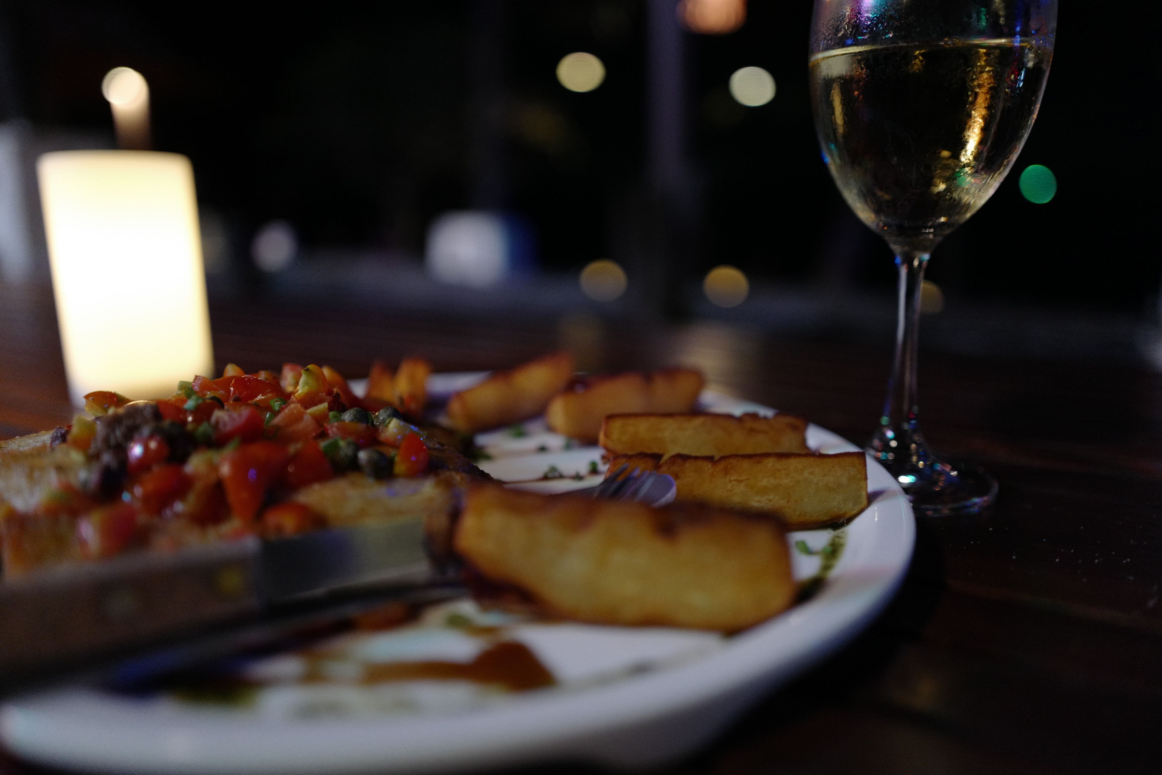 Un plato de comida con pizza y productos fritos, una copa de vino blanco y una vela sobre la mesa.