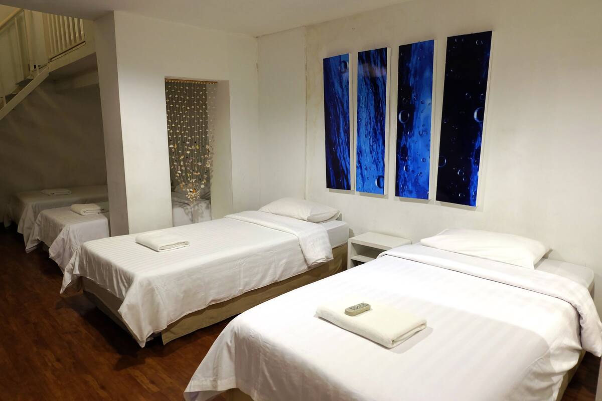 Una habitación de hotel con tres camas individuales, una escalera y una pared con tres grandes cuadros azules.
