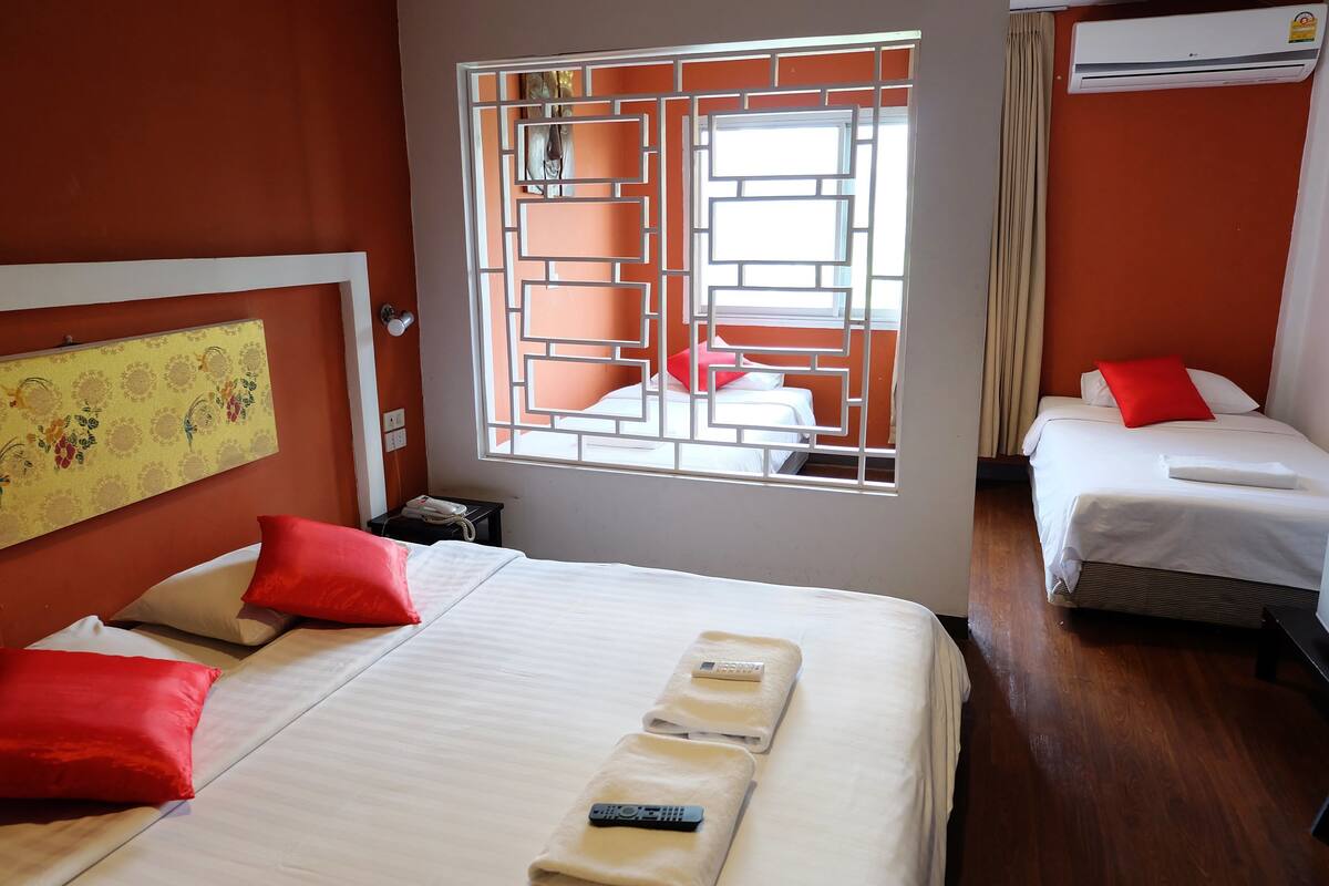 Habitación de hotel con dos camas, almohadas rojas, una ventana con diseño geométrico y un equipo de aire acondicionado.
