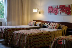 Habitación de hotel con dos camas, ropa de cama a rayas, un teléfono en la mesita de noche, una lámpara y un cuadro con motivos florales en la pared.
