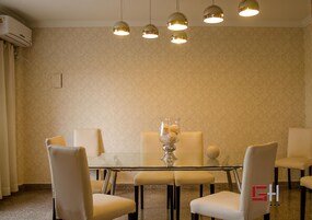 Un comedor con una mesa de vidrio, cuatro sillas, un florero con flores e iluminación colgante.