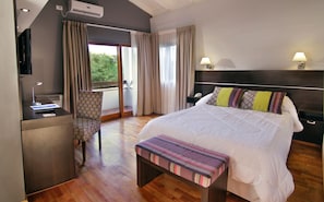 A hotel room with a bed, bedside table, lamp, chair, desk, and an air conditioning unit. - Harmonie Hotel de Montaña (Villa General Belgrano)