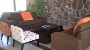 A cozy living area with a stone wall, a brown sofa with an orange pillow, a white chair with polka dots, and a black coffee table. - Harmonie Hotel de Montaña (Villa General Belgrano)