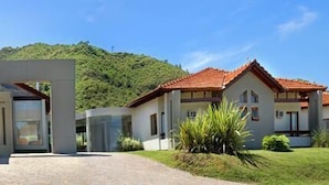 A modern hotel with a central entrance, surrounded by lush greenery and a mountainous backdrop. - Harmonie Hotel de Montaña (Villa General Belgrano)