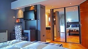 A modern hotel room with a large bed, a flat-screen TV mounted on the wall, and a sliding glass door leading to a balcony. - Harmonie Hotel de Montaña (Villa General Belgrano)