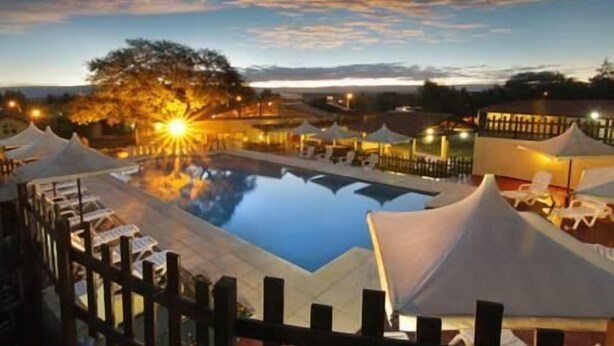 A pool area with lounge chairs and tents, surrounded by buildings and a sunset sky. - Harmonie Hotel de Montaña (Villa General Belgrano)