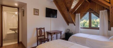 A bedroom with two beds, a wooden ceiling, a TV, a small table, and a window with curtains.