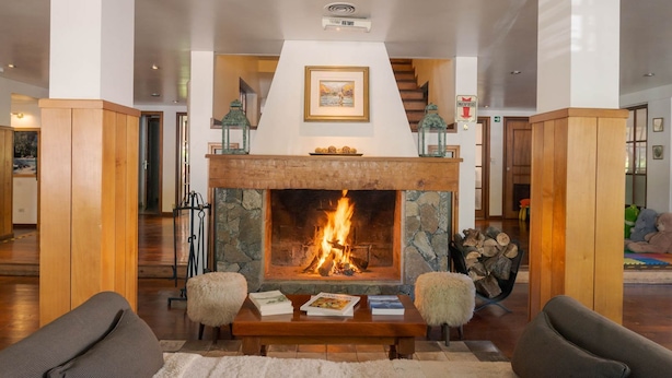 Un salón con chimenea, muebles de madera y una escalera al fondo.