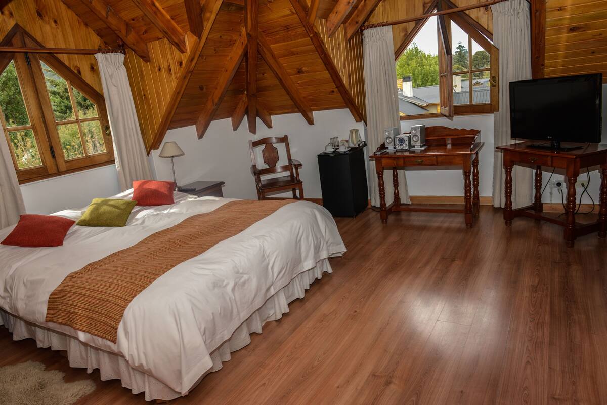 Een slaapkamer met een groot bed, houten plafond, een bureau met computer en een televisie.