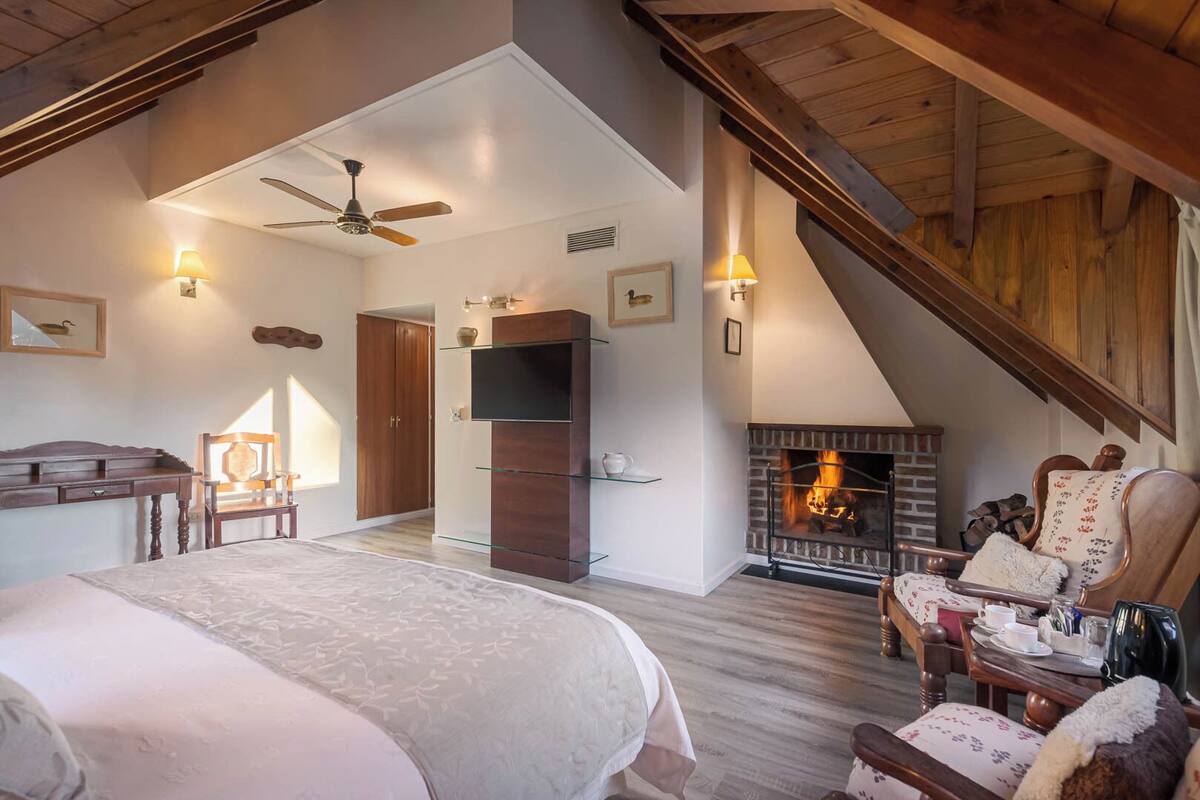 Ruime slaapkamer met een groot bed, een open haard, een houten plafond en een televisie.