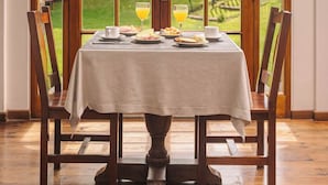Una mesa de comedor con mantel blanco, dos sillas y vistas a un jardín a través de un ventanal arqueado.