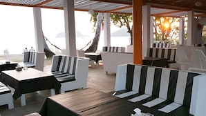 Un área de estar al aire libre con mesas y sillas, piso de madera y vista al mar.