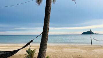 A beach scene with a hammock, a palm tree, and a distant island.