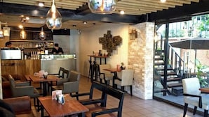 Un café avec des tables et des chaises en bois, des lampes suspendues et un mur en pierre.