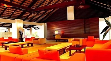 Amplio espacio interior con diversas disposiciones de asientos, incluyendo sofás y una mesa larga, bajo un techo alto con vigas a la vista.