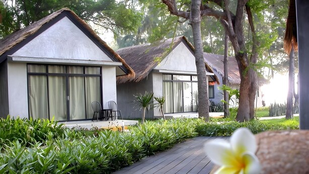 A resort with thatched-roof cottages, a wooden deck, and lush greenery. - Casuarina Beach Resort (Cha Am)