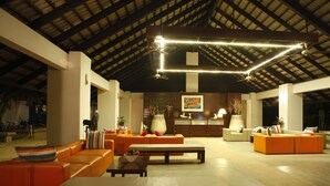 A spacious indoor area with a high ceiling, orange seating, a central table, and a kitchen area in the background. - Casuarina Beach Resort (Cha Am)