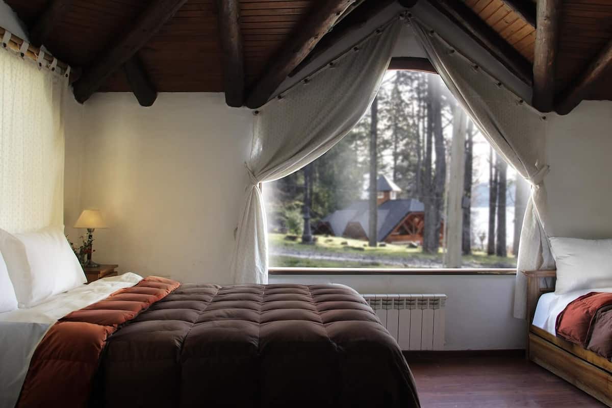 Un dormitorio con dos camas, una ventana con vista a árboles y techo de madera.