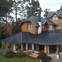 Una cabaña de madera con una gran chimenea, un porche cubierto y cimientos de piedra.