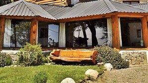 Une cabane en bois avec une cheminée, de grandes fenêtres et une véranda.