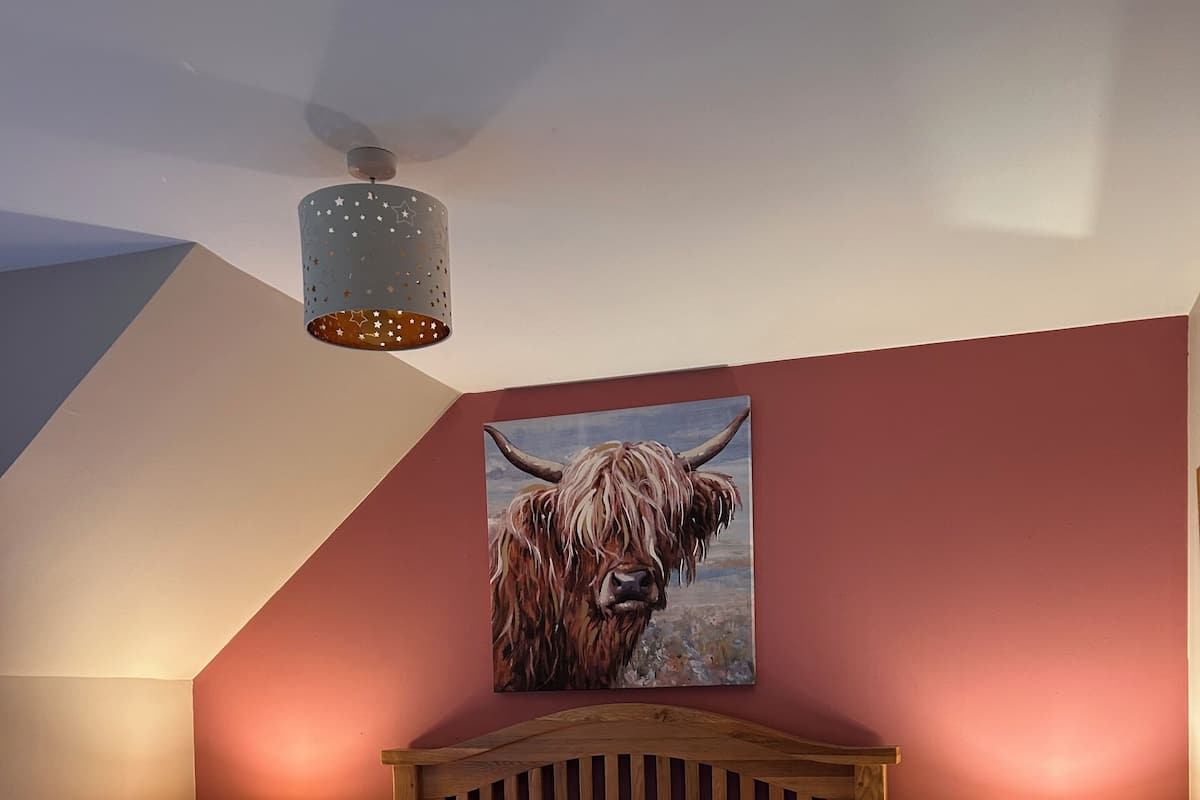 Quarto com cama de madeira, duas mesas de cabeceira com luminárias, ventilador de teto e pintura de um touro na parede.