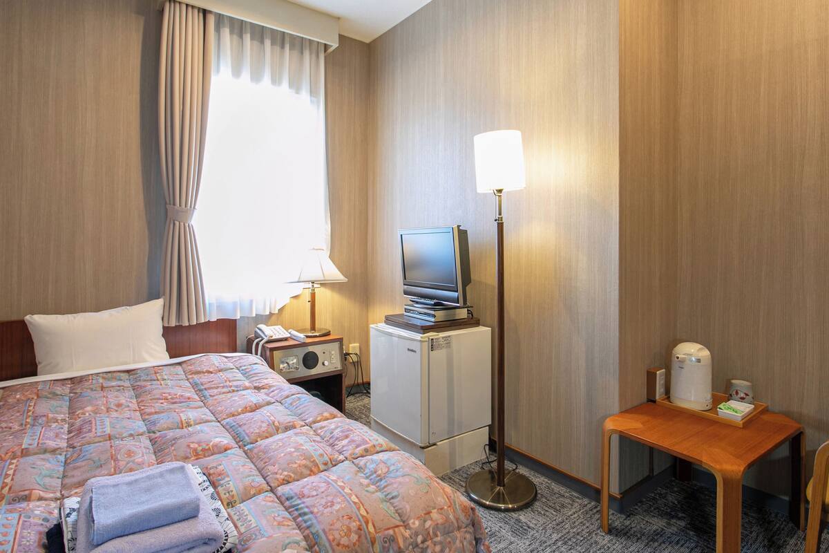 A hotel room with a bed, a desk, a television, a lamp, a coffee maker, and a minibar.