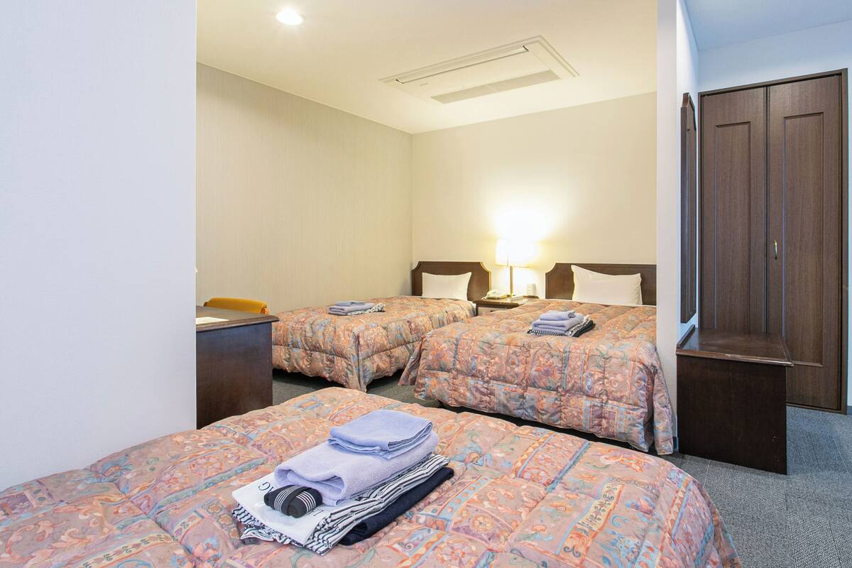 A hotel room with two beds, a desk, a wardrobe, and a nightstand with a lamp.