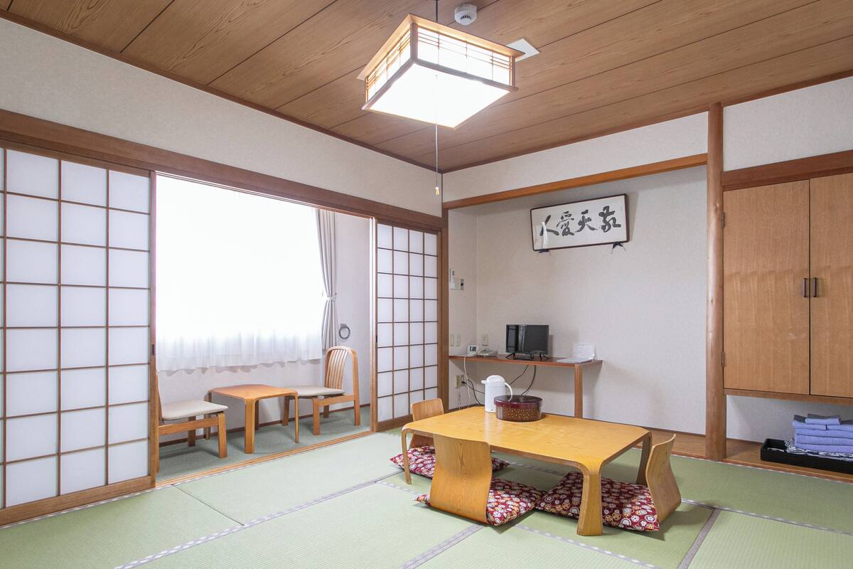A traditional Japanese room with tatami flooring, a low wooden table, a television, and a sliding door.