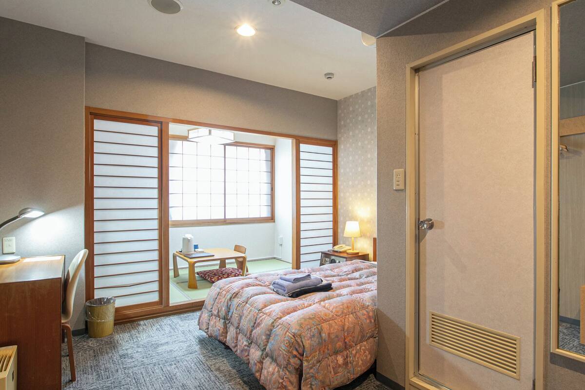 A hotel room with a bed, desk, chair, and a sliding shoji screen door.