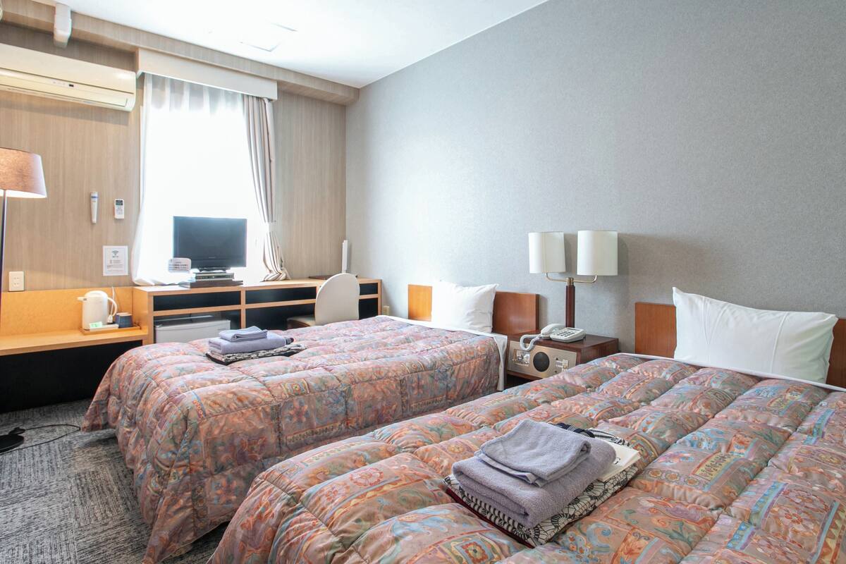 A hotel room with two beds, a desk with a computer, a TV, and a telephone.
