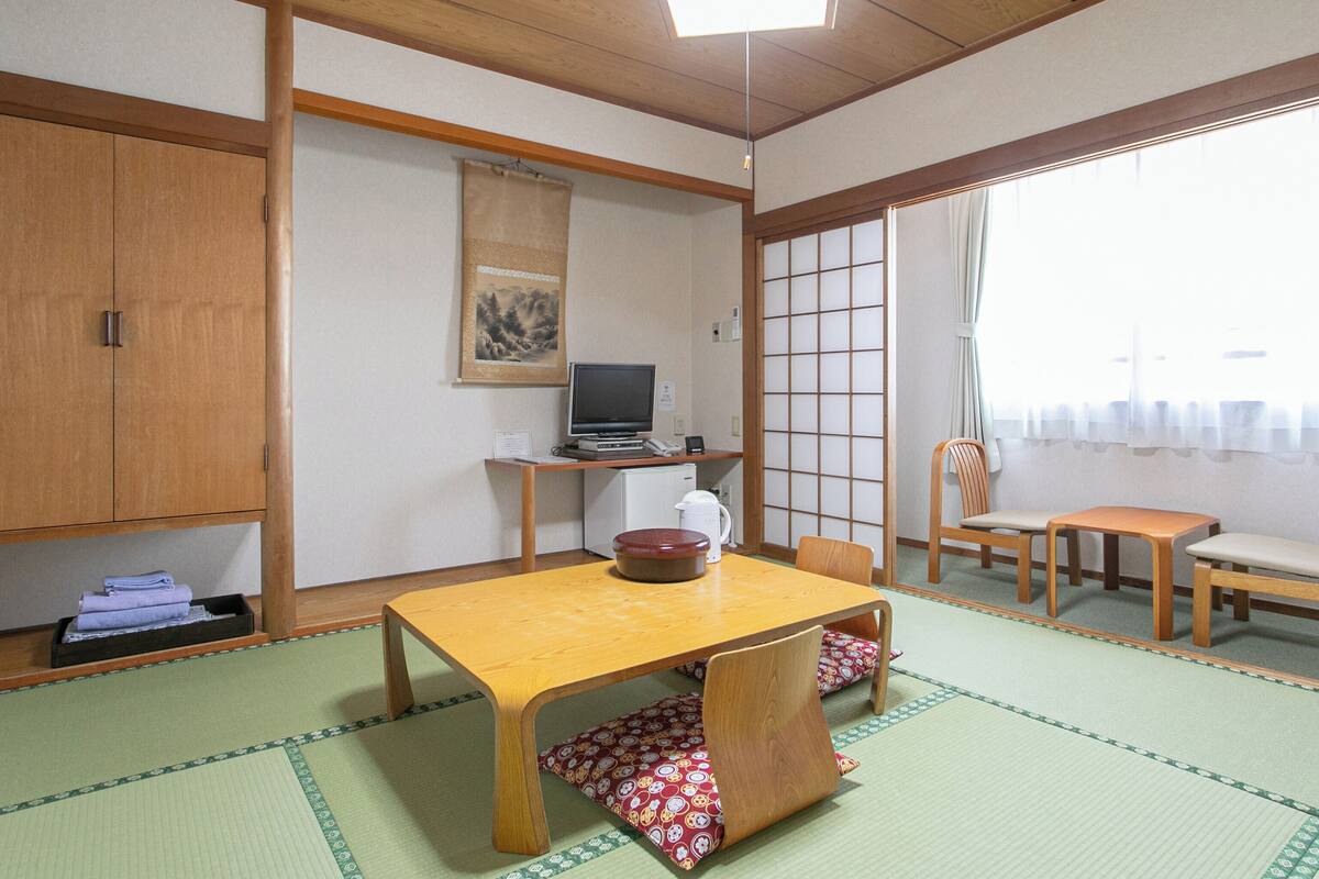 A traditional Japanese room with tatami flooring, a low table, a desk with a computer, and a sliding door.